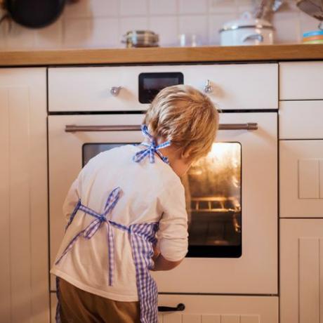 Bambino piccolo che osserva nel forno all'interno, cottura