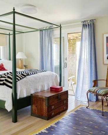 camera degli ospiti, biancheria bianca e giroletto verde con tappeto giallo e blu con cassapanca in legno marrone