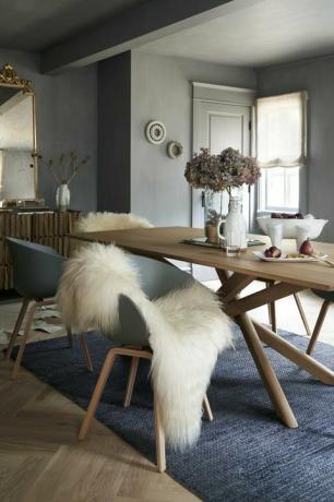 sala da pranzo con tappeto blu e tavolo in legno, sedie blu e tappeto in pelle di pecora, vernice grigia