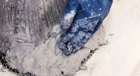 Primo piano immagine di una mano guantata che applica cemento a un telaio di scultura in metallo