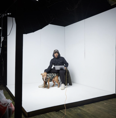 un uomo siede in uno studio fotografico bianco con un cane accanto a lui