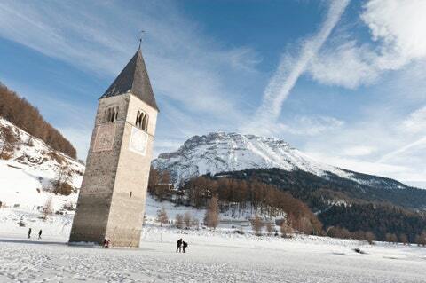 turisti che camminano sul lago ghiacciato di resia, in una soleggiata giornata invernale