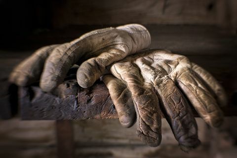 Guanti da lavoro ben usurati, sporchi e oleosi sopra un vecchio banco da lavoro.