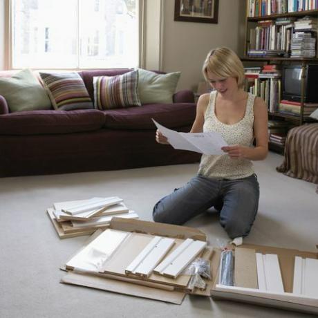 Donna che si inginocchia sul pavimento del suo salotto leggendo le istruzioni per il montaggio dei mobili Flatpack