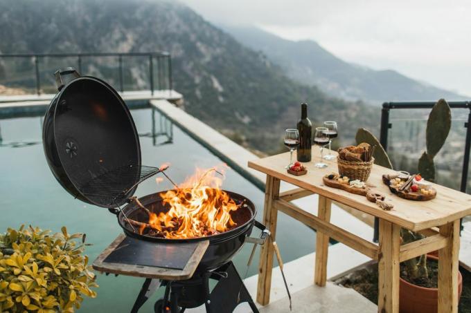 preparazione per una festa barbecue all'aperto di lusso che brucia il fuoco nella griglia, tavolo con snack e vino