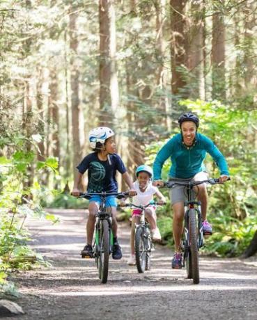 una donna e i suoi due bambini vanno in bicicletta nella foresta sotto il sole