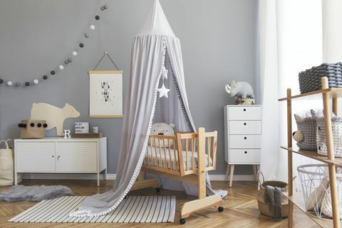 Elegante camera da letto scandinava per neonato con poster mock up, mobili bianchi, giocattoli naturali, baldacchino grigio sospeso con stelle e orsacchiotti. Interno minimalista e accogliente della stanza dei bambini.