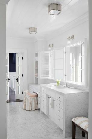 bagno in marmo, ripiani in marmo, piccole piastrelle esagonali in marmo, armadi bianchi, specchio bianco, mobiletto e sgabello