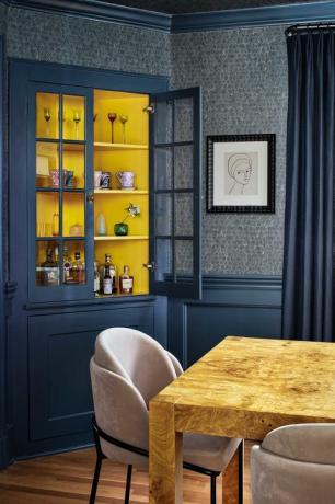 sala da pranzo con pareti dipinte di blu e rivestimento murale blu scuro, mobile bar con alcool, sedia da pranzo in legno con sedie da pranzo in velluto rosa