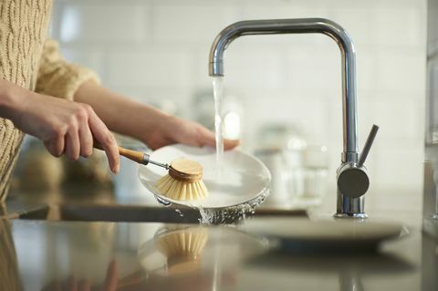 una donna usa una spazzola priva di plastica per pulire i piatti in un lavello da cucina, primo piano