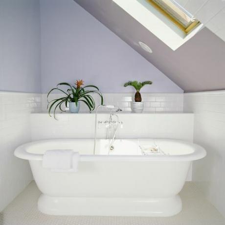 vasca da bagno sotto lucernario in bagno mansardato con pareti viola lilla