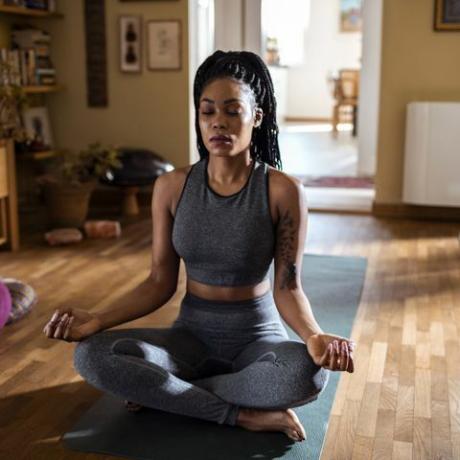 donna nera seduta in una stanza soleggiata meditando nella posa del loto