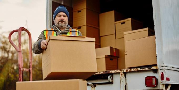 lavoratore di sesso maschile che scarica scatole di cartone dal furgone per le consegne