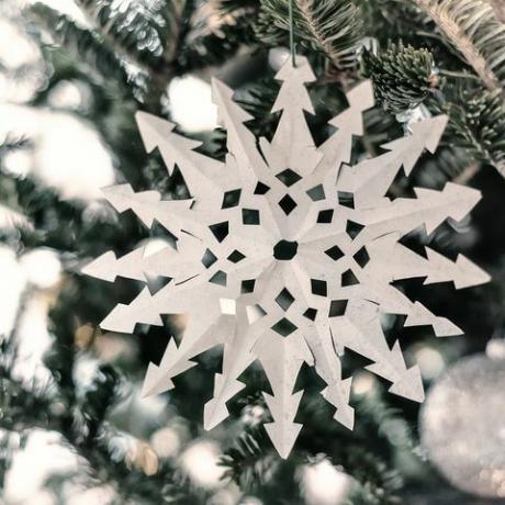 Primo piano di un fiocco di neve di carta bianca appeso a un ramo di albero di Natale