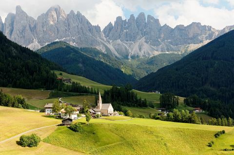 Scenario estivo dell'idilliaca Val di Funes con aspre vette dell'Odle (Geisler) montuosa sullo sfondo e una chiesa nel villaggio di Santa Maddalena nella verde valle erbosa in Dolomiti, Alto Adige, Italia