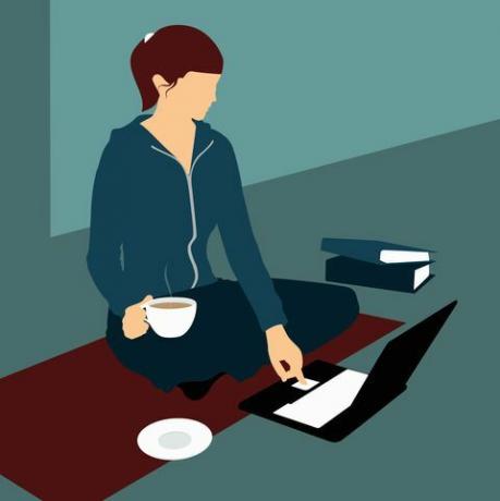 Una donna seduta sul pavimento con una tazza di tè e utilizzando un computer portatile