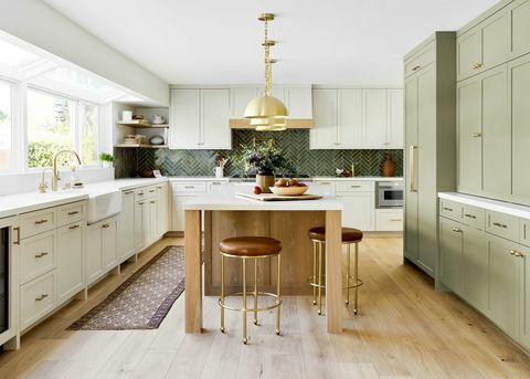 cucina soleggiata con armadi color crema, armadietti verde oliva per riporre oggetti, isola cucina in legno, sgabelli in pelle marrone, hardware dorato