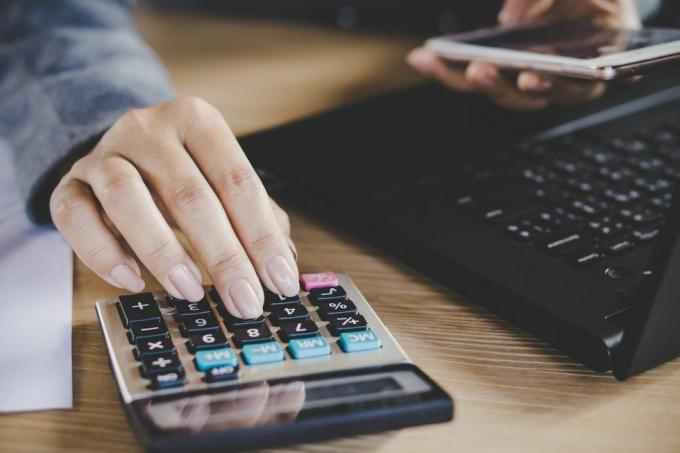 Mano della donna che calcola mentre lavora al computer portatile