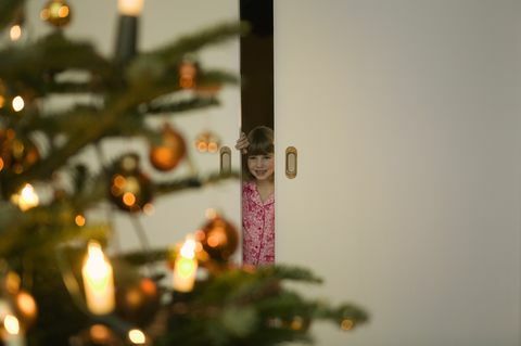 Ragazza in pigiama che scruta attraverso la porta all'albero di Natale