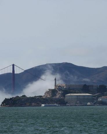 la nebbia bassa turbina intorno ad Alcatraz e al Golden Gate Bridge sotto cieli limpidi mentre le barche salpano sulla baia di San Francisco