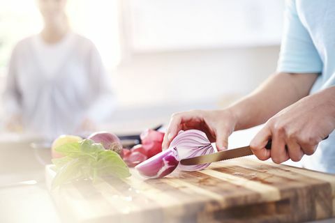 Donna che affetta cipolla rossa sul tagliere in cucina