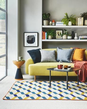 soggiorno, divano giallo, mensola bianca dietro con un tappeto a motivi blu e giallo sul pavimento