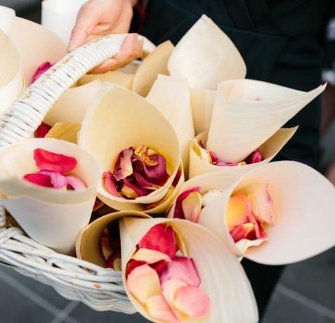 un'immagine ravvicinata di petali di rosa in coni bianchi seduti in un cesto da usare come coriandoli durante una cerimonia di matrimonio